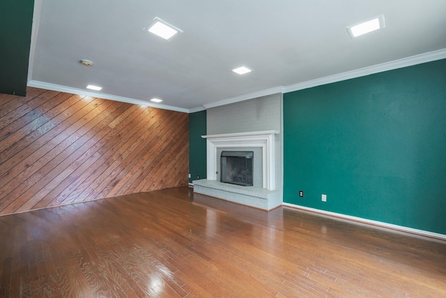 unfurnished living room with wooden walls, a fireplace, ornamental molding, and wood finished floors