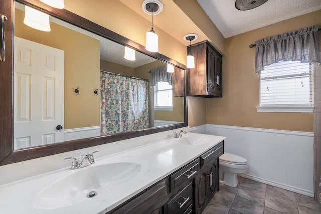 bathroom with a textured ceiling, wainscoting, a sink, and toilet