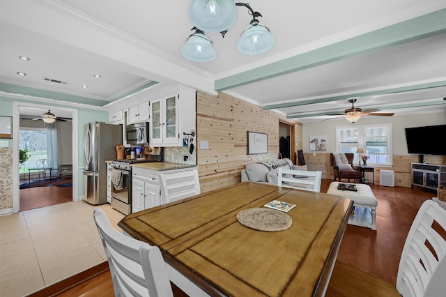 dining space with light tile patterned floors, visible vents, beamed ceiling, crown molding, and wood walls