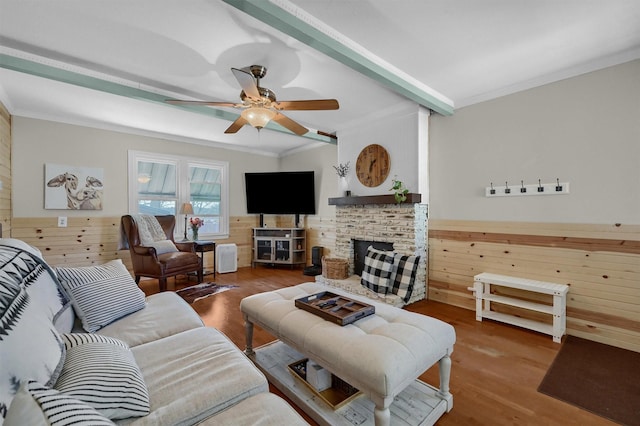 living area featuring wooden walls, a fireplace, wood finished floors, a ceiling fan, and crown molding