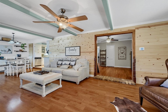 living area featuring crown molding, wood walls, beamed ceiling, and light wood-style floors