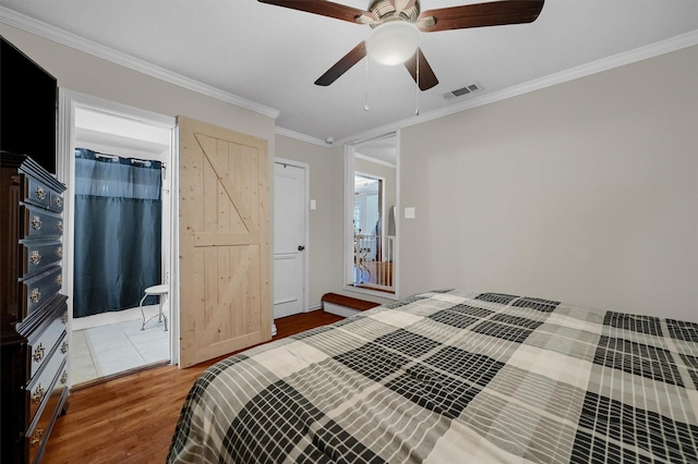 bedroom with visible vents, a barn door, ornamental molding, ceiling fan, and wood finished floors