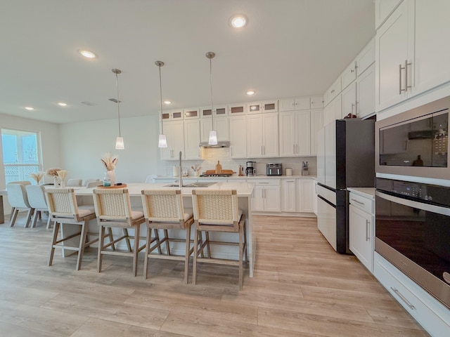 kitchen featuring a breakfast bar area, stainless steel appliances, light wood-style floors, light countertops, and decorative backsplash