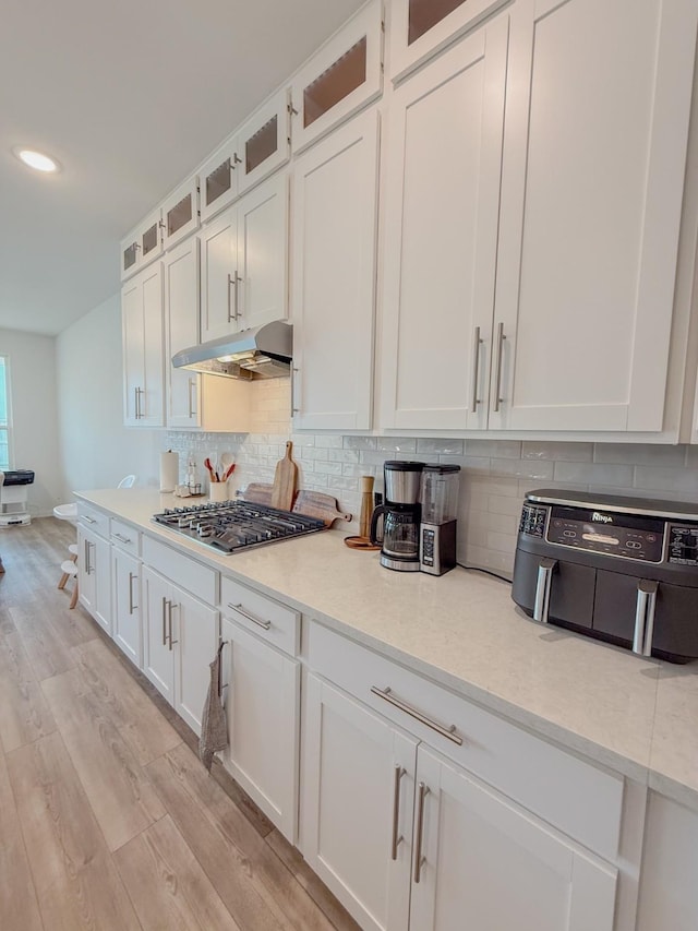 kitchen featuring tasteful backsplash, white cabinets, light wood-style floors, under cabinet range hood, and stainless steel gas cooktop