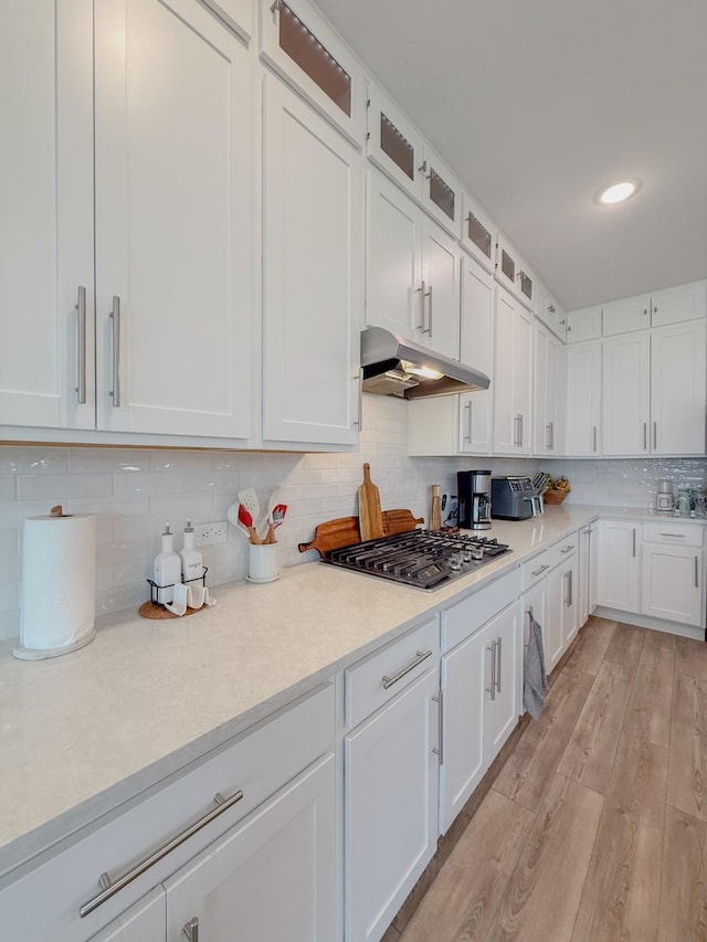 kitchen with white cabinets, light wood-style flooring, glass insert cabinets, under cabinet range hood, and stainless steel gas cooktop