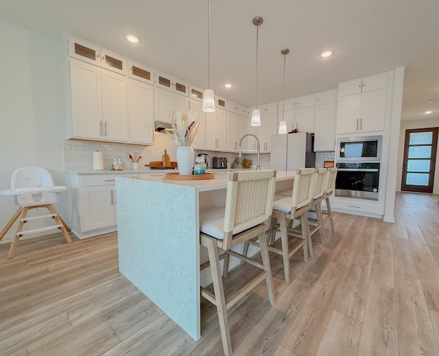 kitchen featuring stainless steel appliances, tasteful backsplash, light countertops, light wood-style flooring, and white cabinets