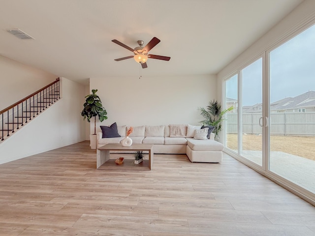 living room with visible vents, ceiling fan, light wood-style flooring, and stairs