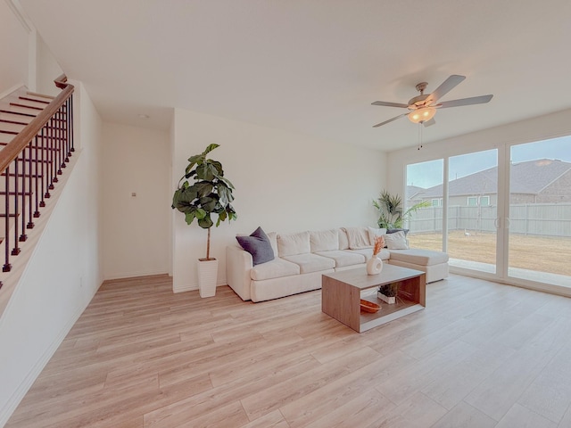 living area with light wood finished floors, stairs, baseboards, and a ceiling fan