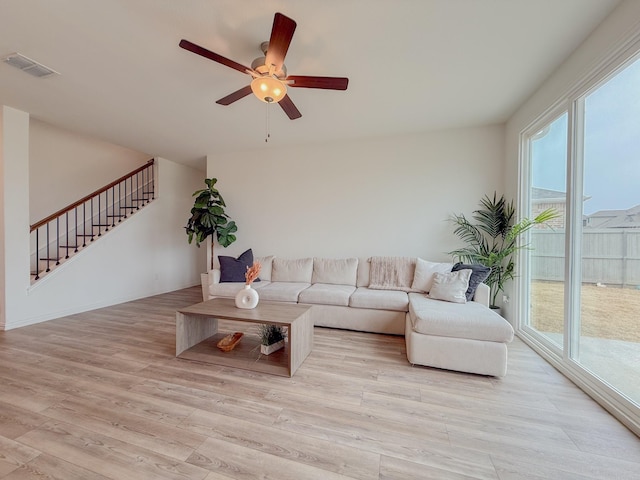 living room with light wood-style floors, stairs, visible vents, and a ceiling fan