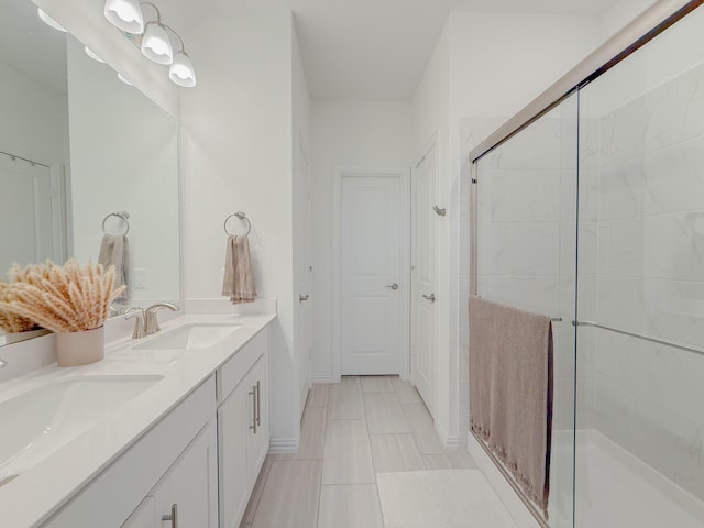 full bath with double vanity, a stall shower, baseboards, and a sink