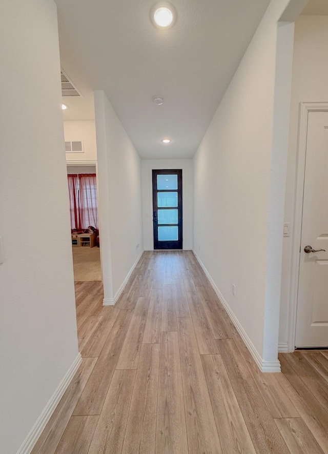 hallway featuring visible vents, light wood-style flooring, and baseboards