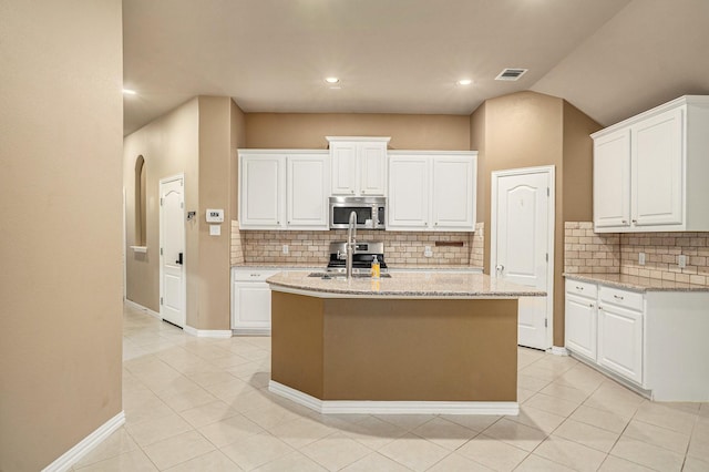 kitchen with light stone countertops, a kitchen island with sink, arched walkways, a sink, and appliances with stainless steel finishes