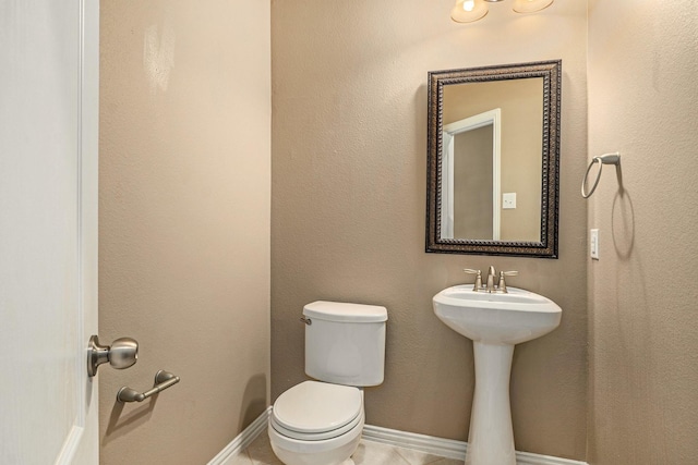 half bathroom featuring tile patterned floors, toilet, and baseboards