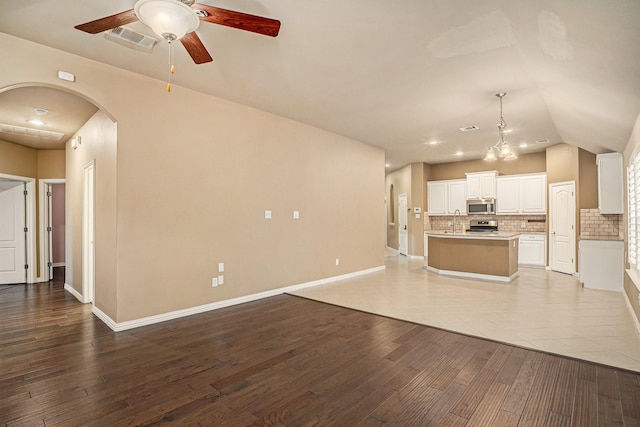 unfurnished living room with visible vents, wood finished floors, arched walkways, baseboards, and ceiling fan