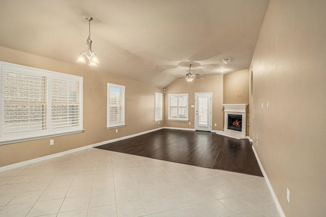 unfurnished living room featuring baseboards, lofted ceiling, a warm lit fireplace, and ceiling fan with notable chandelier