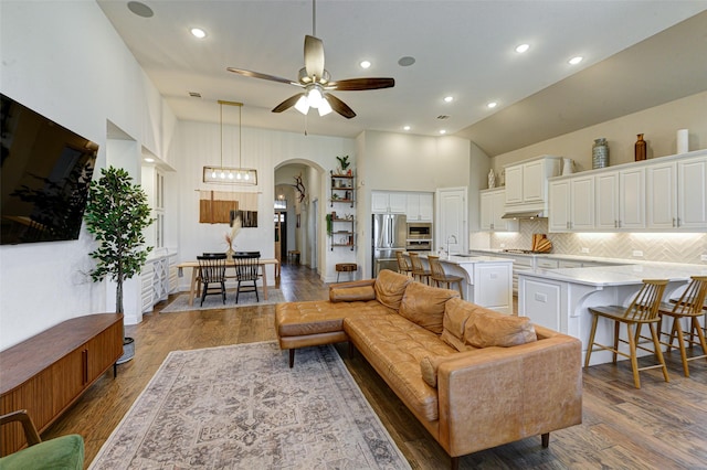 living room with arched walkways, high vaulted ceiling, wood finished floors, and a ceiling fan