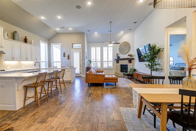 dining room featuring dark wood-type flooring, lofted ceiling, a healthy amount of sunlight, and a stone fireplace