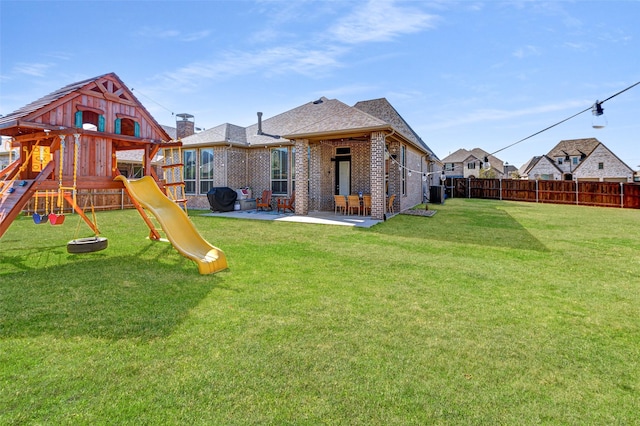 back of house featuring a lawn, a patio, a fenced backyard, a playground, and brick siding