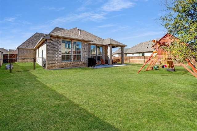 back of property featuring a playground, a yard, brick siding, a patio area, and a fenced backyard