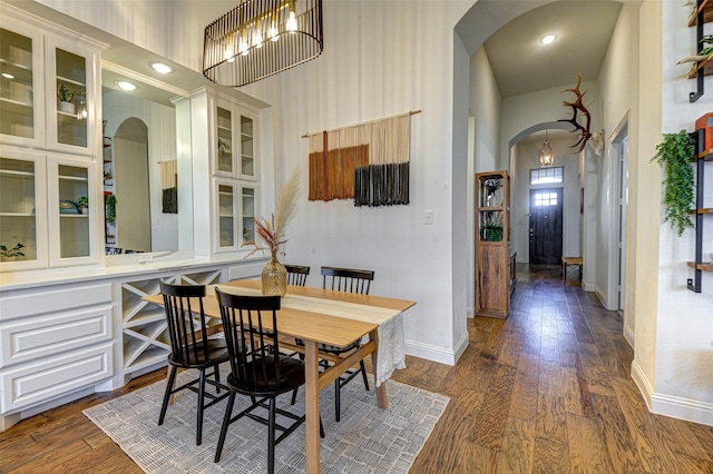 dining room featuring a towering ceiling, baseboards, arched walkways, and dark wood-style flooring