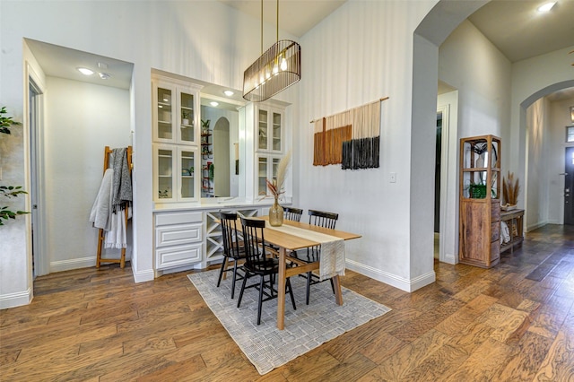 dining area with arched walkways, a high ceiling, baseboards, and wood finished floors