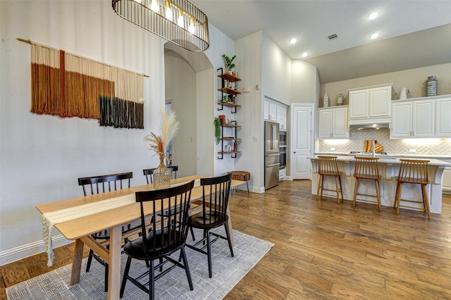 dining area featuring baseboards, visible vents, wood finished floors, high vaulted ceiling, and recessed lighting