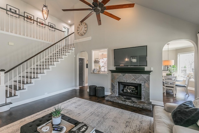 living area with arched walkways, wood finished floors, a tile fireplace, and stairs