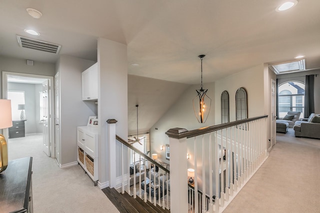 corridor with light carpet, plenty of natural light, visible vents, and an upstairs landing