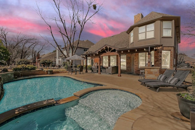 pool at dusk featuring a pool with connected hot tub and a patio