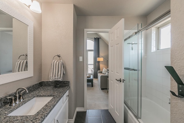 bathroom featuring a textured wall, baseboards, combined bath / shower with glass door, and vanity