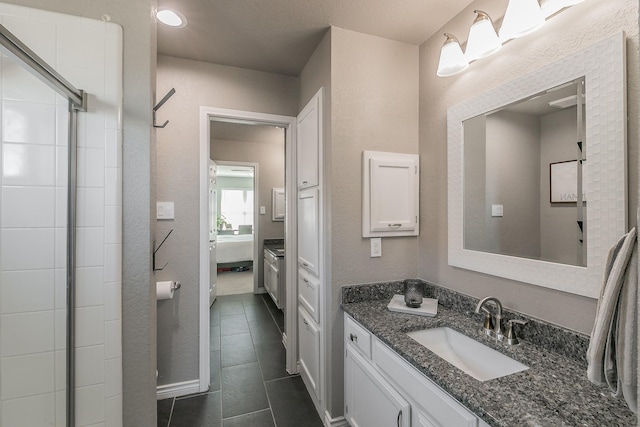 ensuite bathroom with connected bathroom, a textured wall, a shower with shower door, tile patterned flooring, and vanity