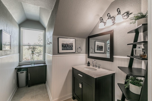 bathroom with wainscoting, vaulted ceiling, a textured ceiling, vanity, and tile patterned flooring