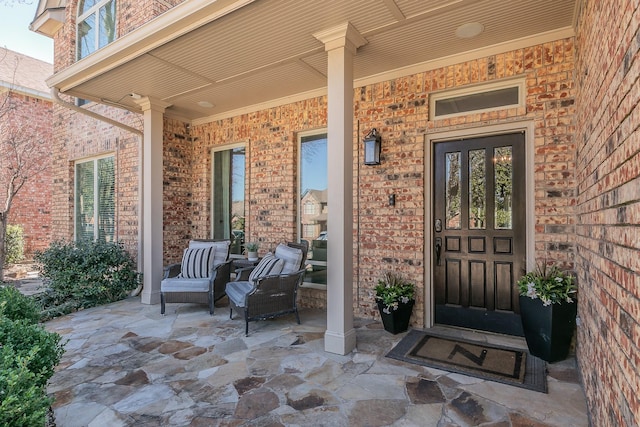 view of exterior entry featuring covered porch and brick siding