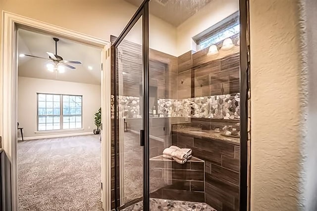 bathroom with a textured wall, a ceiling fan, baseboards, vaulted ceiling, and a tile shower