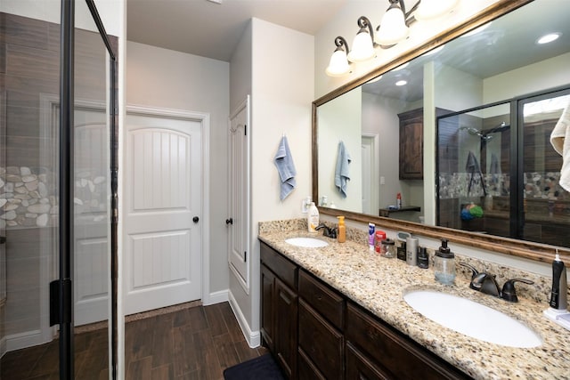 bathroom with double vanity, a sink, a shower stall, and wood finished floors