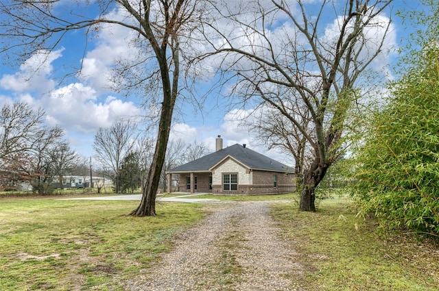 view of front of property featuring driveway, a chimney, a front lawn, and brick siding