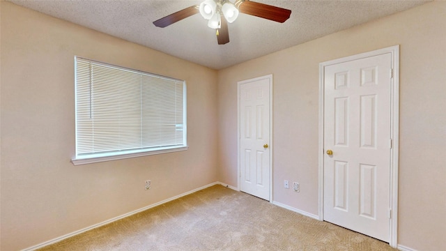 unfurnished bedroom with light colored carpet, ceiling fan, a textured ceiling, and baseboards