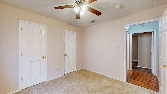 unfurnished bedroom with baseboards, visible vents, a ceiling fan, light colored carpet, and a textured ceiling