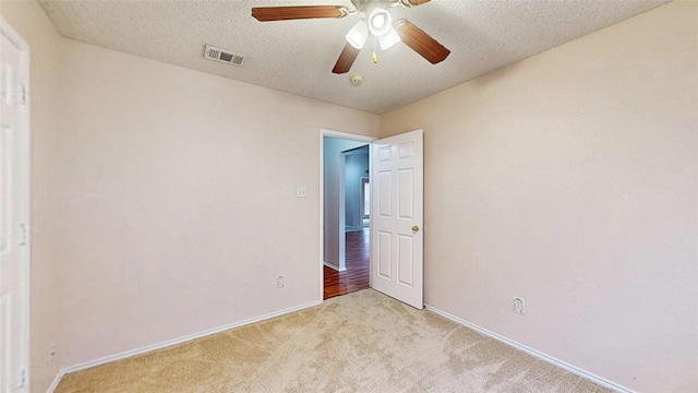 carpeted spare room with a ceiling fan, visible vents, a textured ceiling, and baseboards