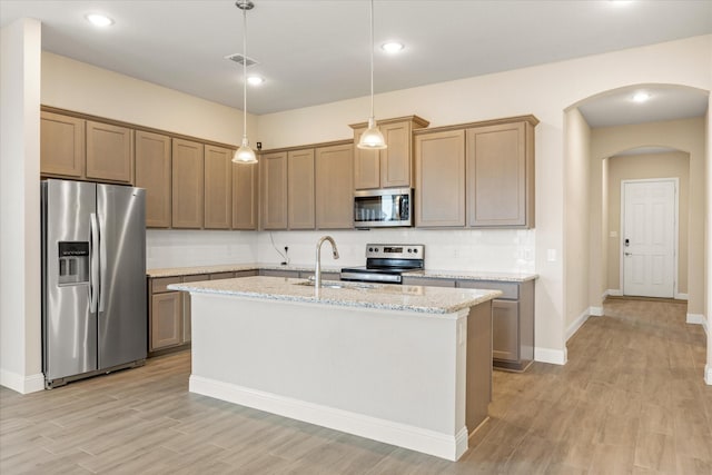 kitchen featuring arched walkways, backsplash, light wood-style flooring, appliances with stainless steel finishes, and a sink