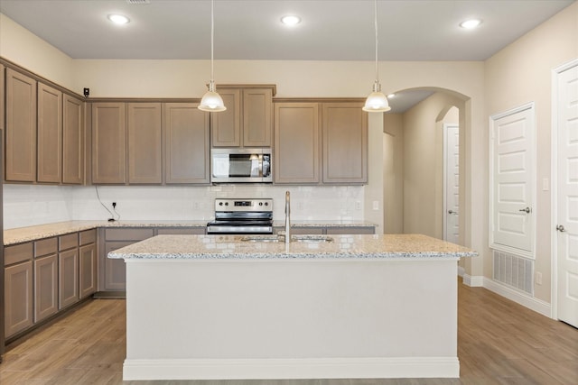 kitchen featuring arched walkways, backsplash, appliances with stainless steel finishes, light wood-style floors, and a sink