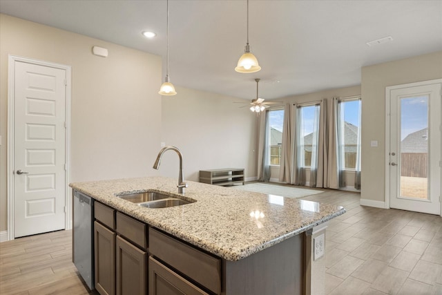 kitchen with dishwasher, hanging light fixtures, light stone countertops, a kitchen island with sink, and a sink