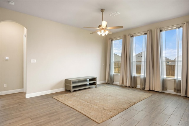 unfurnished room featuring baseboards, visible vents, arched walkways, a ceiling fan, and light wood-style flooring