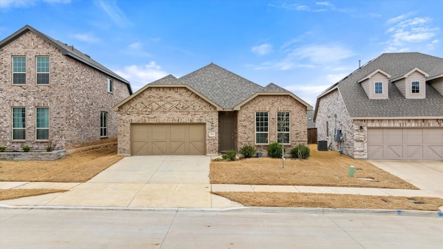 french country style house with driveway, an attached garage, roof with shingles, and brick siding