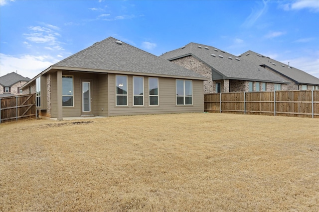 back of house with a fenced backyard, a lawn, and roof with shingles