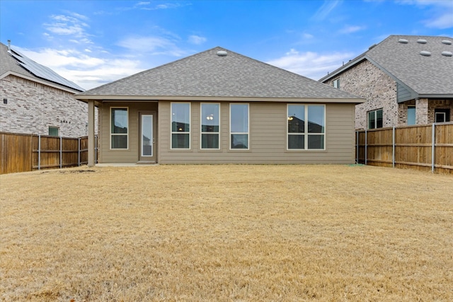 rear view of house featuring a shingled roof, a fenced backyard, and a yard