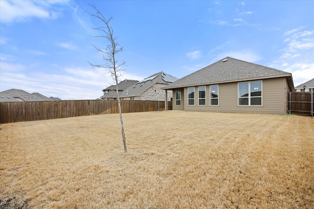 back of house with a shingled roof, a fenced backyard, and a lawn