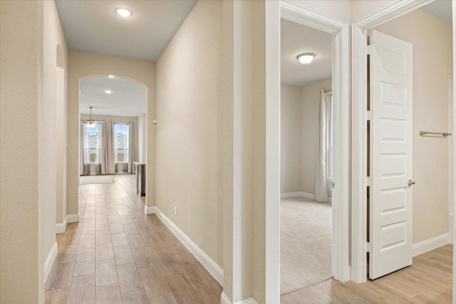 corridor with light wood-style flooring, arched walkways, and baseboards