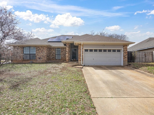 ranch-style house featuring concrete driveway, an attached garage, fence, roof mounted solar panels, and brick siding