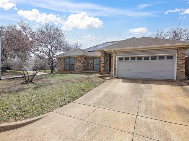 single story home with a garage, concrete driveway, brick siding, and roof mounted solar panels